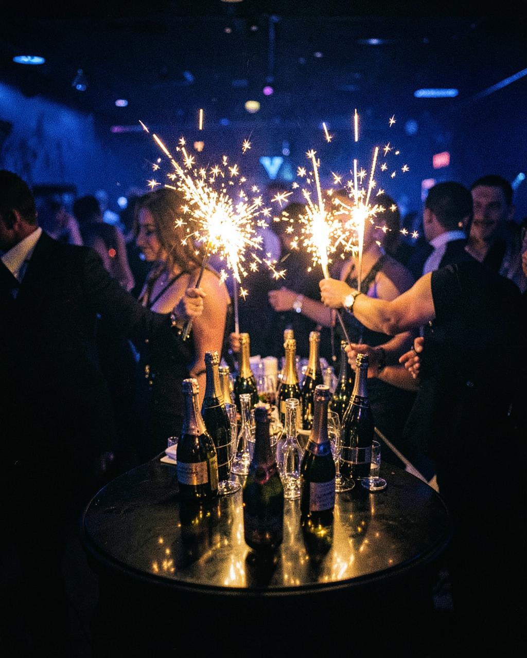 Champagne bottles with sparklers carried to a VIP table in a dark club